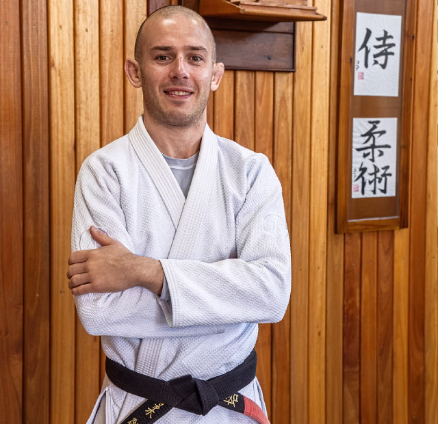 Foto do professor Mateus de pé em frente a um fundo de madeira.