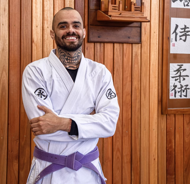 Foto do instrutor Túlio de pé em frente a um fundo de madeira.